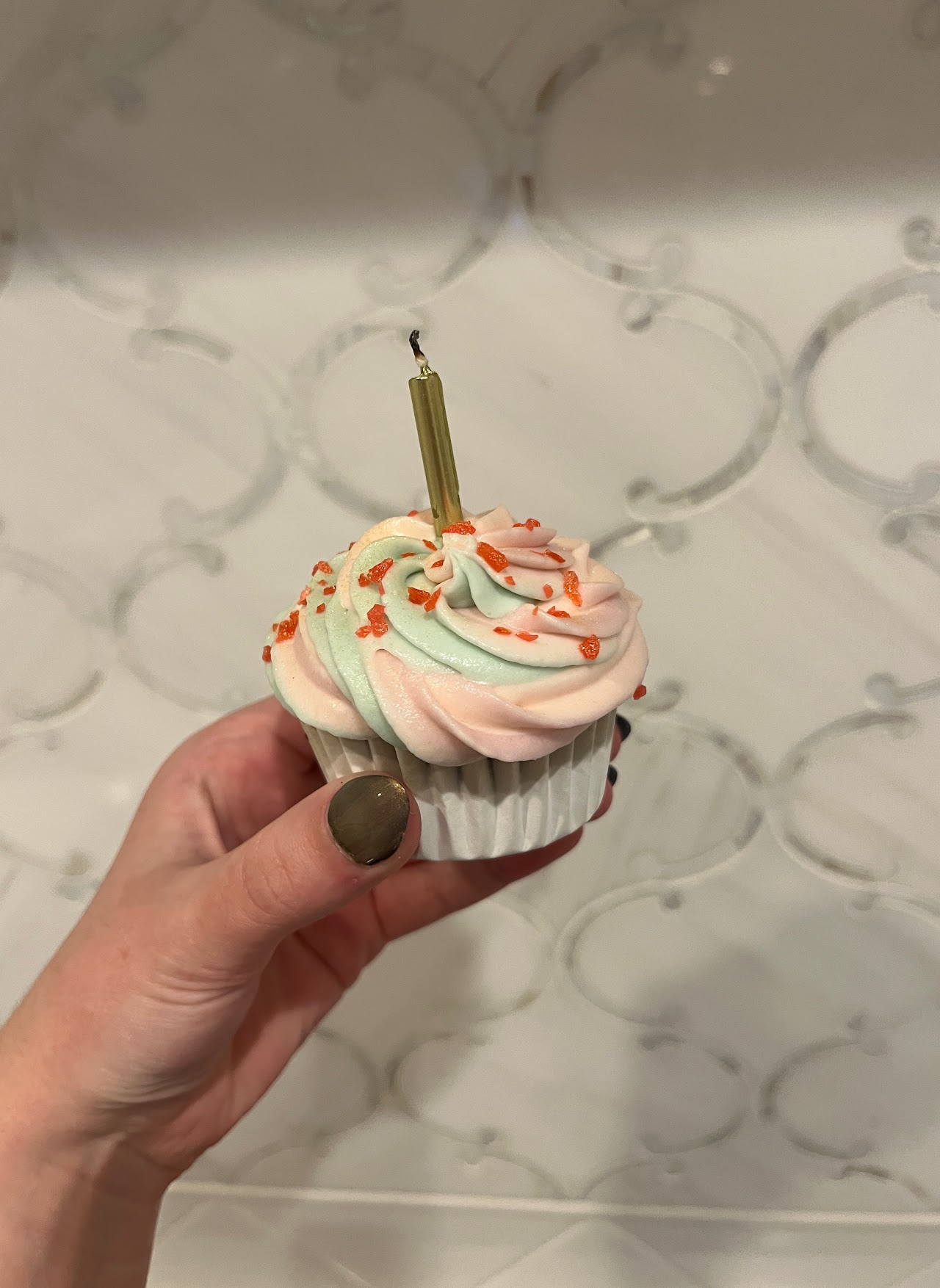 Single cupcake with swirled mint and blush buttercream piping, edible glitter shards, and a gold candle