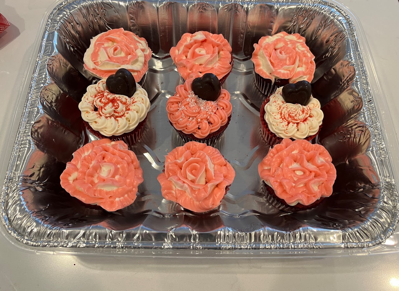 Tray of nine red velvet cupcakes with pink rose piping, white shell piping, and dark chocolate heart toppers