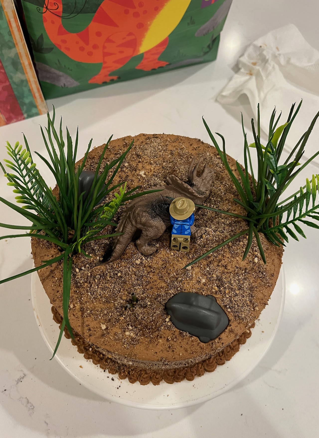 Chocolate buttercream cake styled as a dig site with a sculpted fondant triceratops skull and a toy paleontologist figure