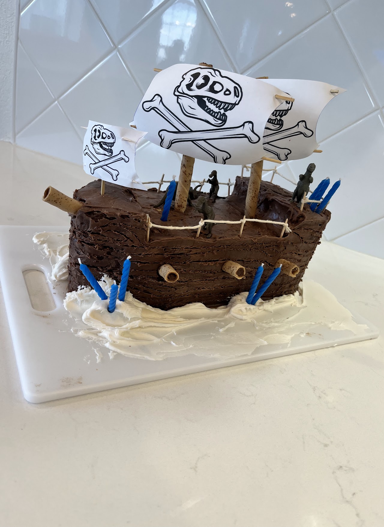 Chocolate buttercream pirate ship cake with printed dinosaur skull and crossbones flags and toy dinosaurs on deck