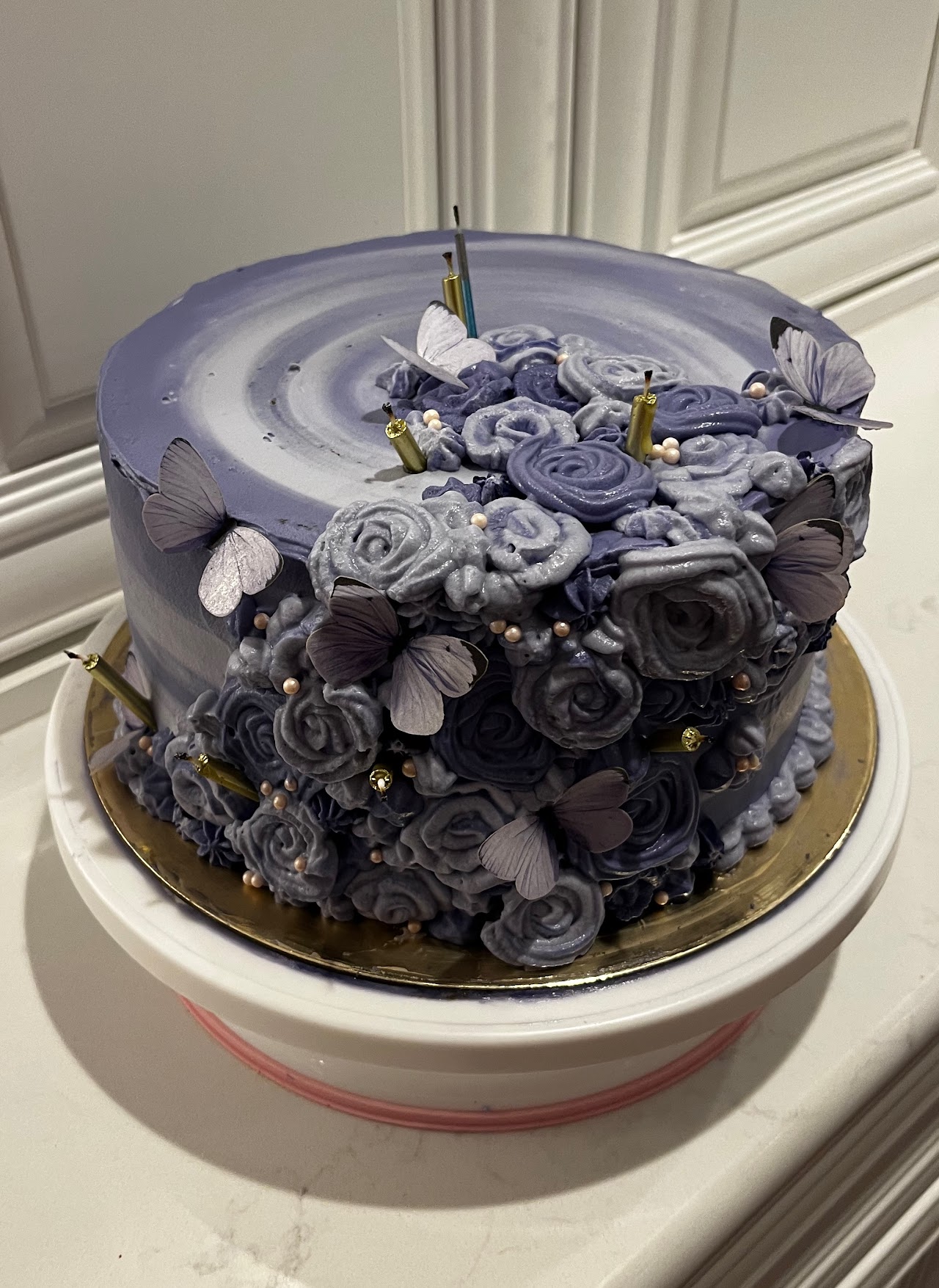 Tall round cake covered in dusty blue piped buttercream roses with sugar butterflies and pearl accents